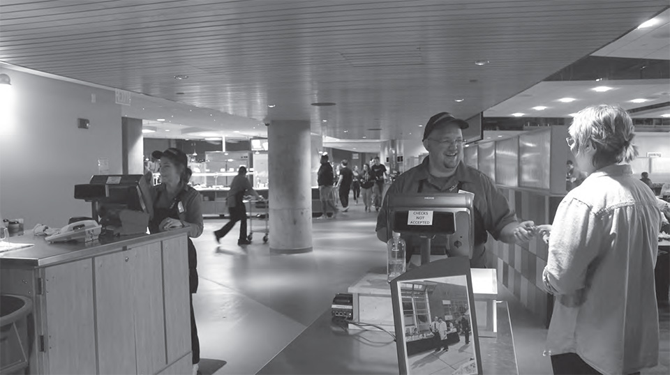 Two dining services employees greet students at the entrance to Riverside Commons, currently being managed by Sodexo.
